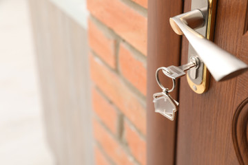 Key with house-shaped trinket in door lock, closeup. Space for text