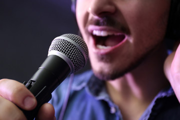 Young singer with microphone recording song in studio, closeup