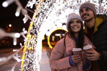 Young couple with cups of mulled wine at winter fair. Space for text