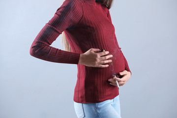 Young pregnant woman smoking cigarette on grey background, closeup. Harm to unborn baby