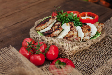 a plate of cooked meat, cheese and vegetables on a wooden table. Near tablecloth from burlap fabric