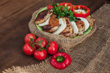 a plate of cooked meat, cheese and vegetables on a wooden table. Near tablecloth from burlap fabric