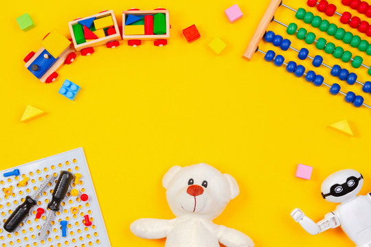 Kids toys background. Teddy bear, wooden train, robot, colorful blocks, toy tools kit, abacus on yellow background