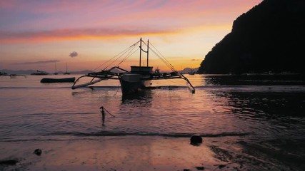 Gimbal steadycam shot of traditional philippine boats bangka at sunset. Beautiful sunset with silhouettes of philippine boats, El Nido, Palawan island, Philippines. Orange sky sunset paradise beach.