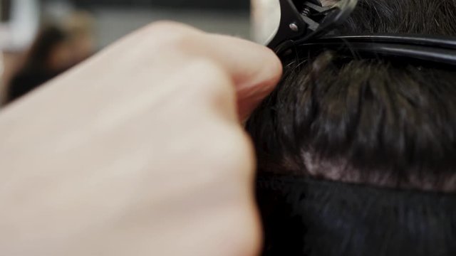 The hairdresser sews artificial hair to the real thing. The process of hair extension. 4K