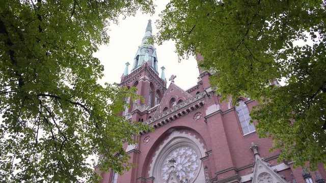 Static shot of the twin towers on St Johns Church, filmed under green leaves and branches, on a cloudy, summer day, in Ullanlinna, Helsinki, Finland