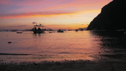 Gimbal steadycam shot of traditional philippine boats bangka at sunset. Beautiful sunset with silhouettes of philippine boats, El Nido, Palawan island, Philippines. Orange sky sunset paradise beach.