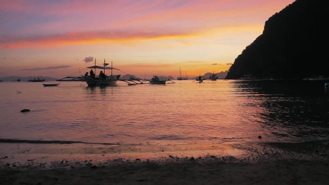 Gimbal steadycam shot of traditional philippine boats bangka at sunset. Beautiful sunset with silhouettes of philippine boats, El Nido, Palawan island, Philippines. Orange sky sunset paradise beach.