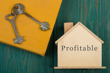 privacy concept - little house with text "Profitable", book and key on blue wooden desk