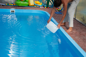 men's hands pour light liquid from a plastic tank into a pool, into water. chemical water purification, alkali balance, unsanitary conditions. disinfection and preparation for swimming