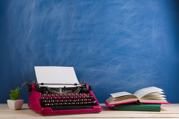 writer's workplace - crimson typewriter and books on blue blackboard background