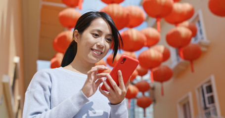 Woman use of cellphone for sending red packet with mobile app over red lantern background