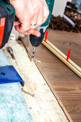 Man using drill machine while installing new wooden laminate flooring at home.