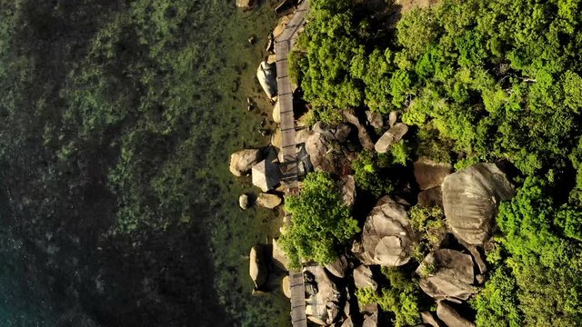 Top view drone shot over a pathway mad eof wood, betweeen the ocean and rocks