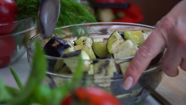 Women's hands mix with a spoon vegetables in a transparent plate.