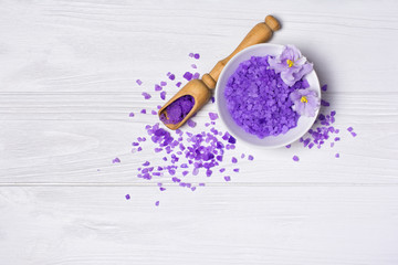 Flavored purple sea salt crystals with violet flower and wooden scoop on white