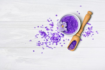 Flavored purple sea salt crystals with violet flower and wooden scoop on white