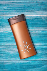 Bronze bottle with sunscreen on blue background as concept of vacation time
