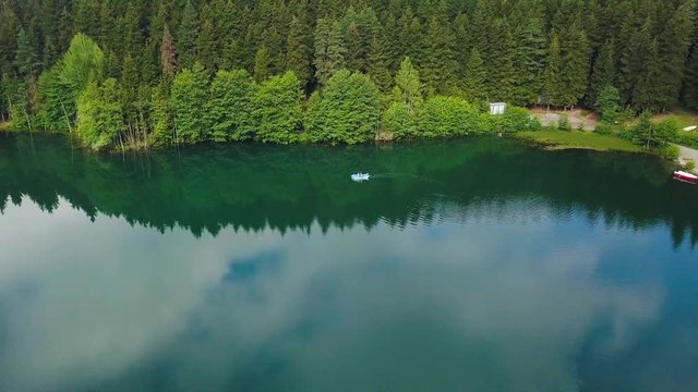 aerial drone shot flying top down, over dark lake, a boat in the lake, lake reflecting blistering forest, a path nearby, in Karagol National Park, Savsat, Turkey