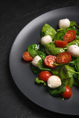 Salad with mozzarella and baby spinach on black ceramic plate