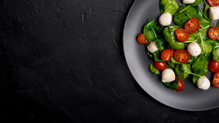 Salad with mozzarella and baby spinach on black ceramic plate. Copy space