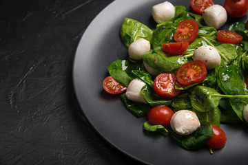 Salad with mozzarella and baby spinach on black ceramic plate