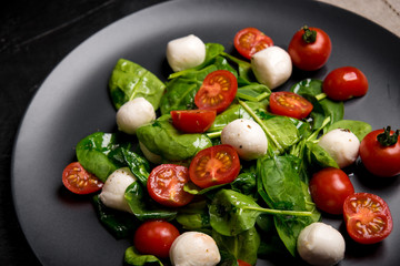 Salad with mozzarella and baby spinach on black ceramic plate