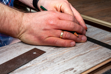 Man using measuring elbow and pencil while installing new wooden laminate flooring at home.