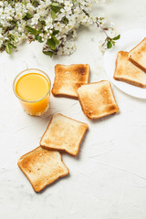 Glass of Fresh Orange Juice, Toast and Branch Spring Flowers on the Light Stone Background. The concept of a Healthy Breakfast