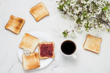 White Cup with Black Coffee, Toast, Jem and Spring Flowers on the Light Stone Background. The concept of a Healthy Breakfast. Flat lay, top view