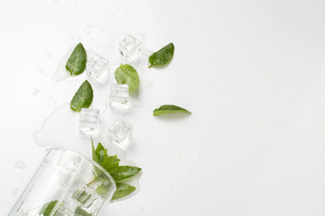 Fototapeta na wymiar Spilled Glass with refreshing water, mint leaves and ice cubes on a light background