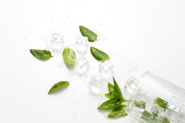 Spilled Glass with refreshing water, mint leaves and ice cubes on a light background