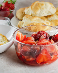 Bowl of sliced strawberries glazed with sugar.  Pastries, sugar, and whole strawberries blurred in the background.