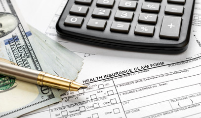 Calculator with money on health insurance claim form. Close up.