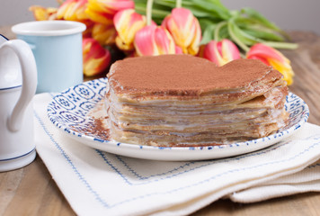 Two cups of aromatic coffee and pancakes with cream. Breakfast for two on a wooden background and a bouquet of red spring tulips. Free space for text.