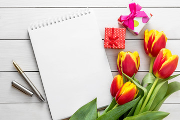Blank notepad with tulips and gift boxes on white wooden table. Space for text.