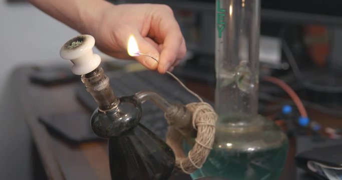 Hemp wick around the base of a bong is lit and held to a bowl of cannabis.