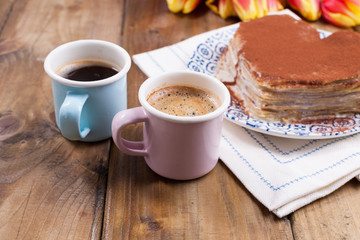 Two cups of aromatic coffee and pancakes with cream. Breakfast for two on a wooden background. Free space for text.
