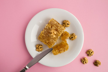 Honeycomb and walnuts in the white plate on the pink background.Beekeeping  products.Top view.