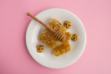 Honeycomb and walnuts in the white plate on the pink background.Beekeeping  products.Top view.