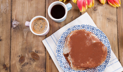 Two cups of aromatic coffee and pancakes with cream. Breakfast for two on a wooden background and a bouquet of red spring tulips. Free space for text.