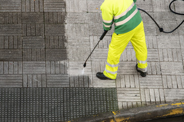 Worker cleaning the street sidewalk with high pressure water jet