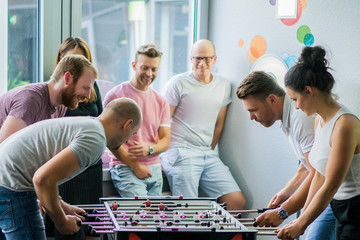 happy managers playing table football at office and having fun together