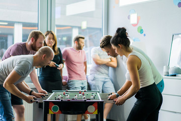 happy managers playing table football at office and having fun together