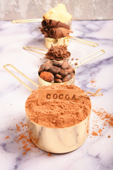 Cocoa, cocoa butter and cocoa beans, chocolate in gold containers on a marble surface. Flat lay. Place for text.