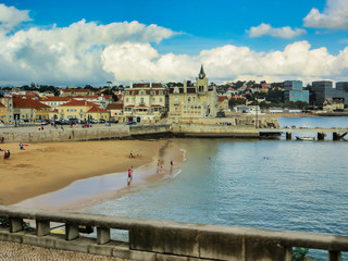The beachfront at Cascais Portugal with a church and old houses by the beach and modern buildings in the background.