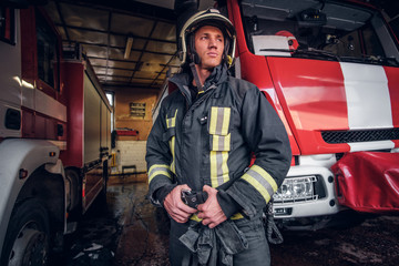 Portrait of a brave young fireman wearing protective uniform standing next to a fire engine in a...