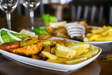 Traditional Mediterranean food. Two plates and glasses on the table in the restaurant. Baked fish and barbecue with vegetable garnish.