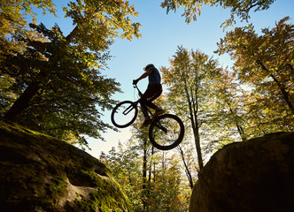 Young male biker jumping on trial bicycle between two big boulders, professional rider making...