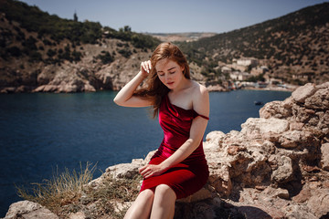 Fototapeta na wymiar A beautiful red-haired woman is sitting on a rock